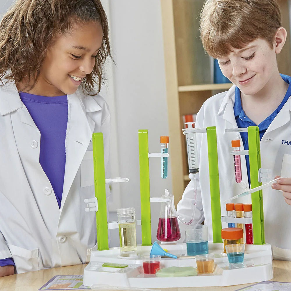 Two children in lab coats conducting a science experiment with colorful liquids in test tubes.